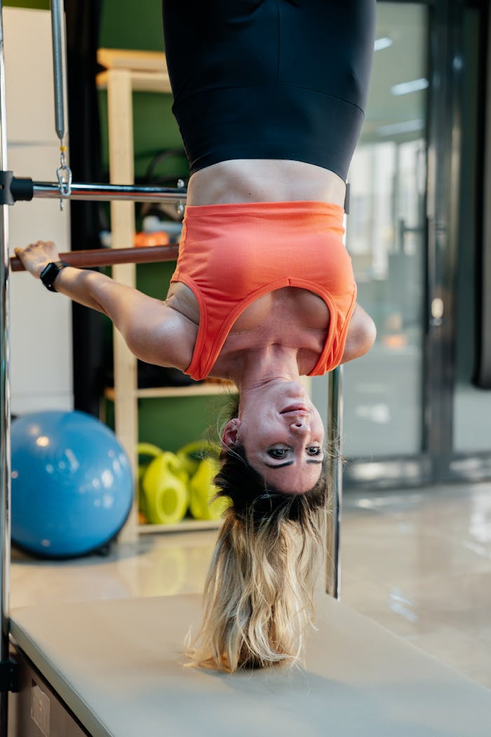 Adult woman performing an upside down pilates exercise on equipment in a gym setting.