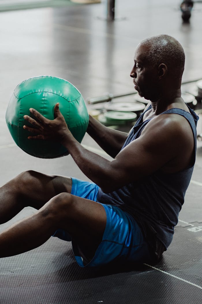 Focused mature man working out with a medicine ball in a gym setting, showcasing strength and determination.